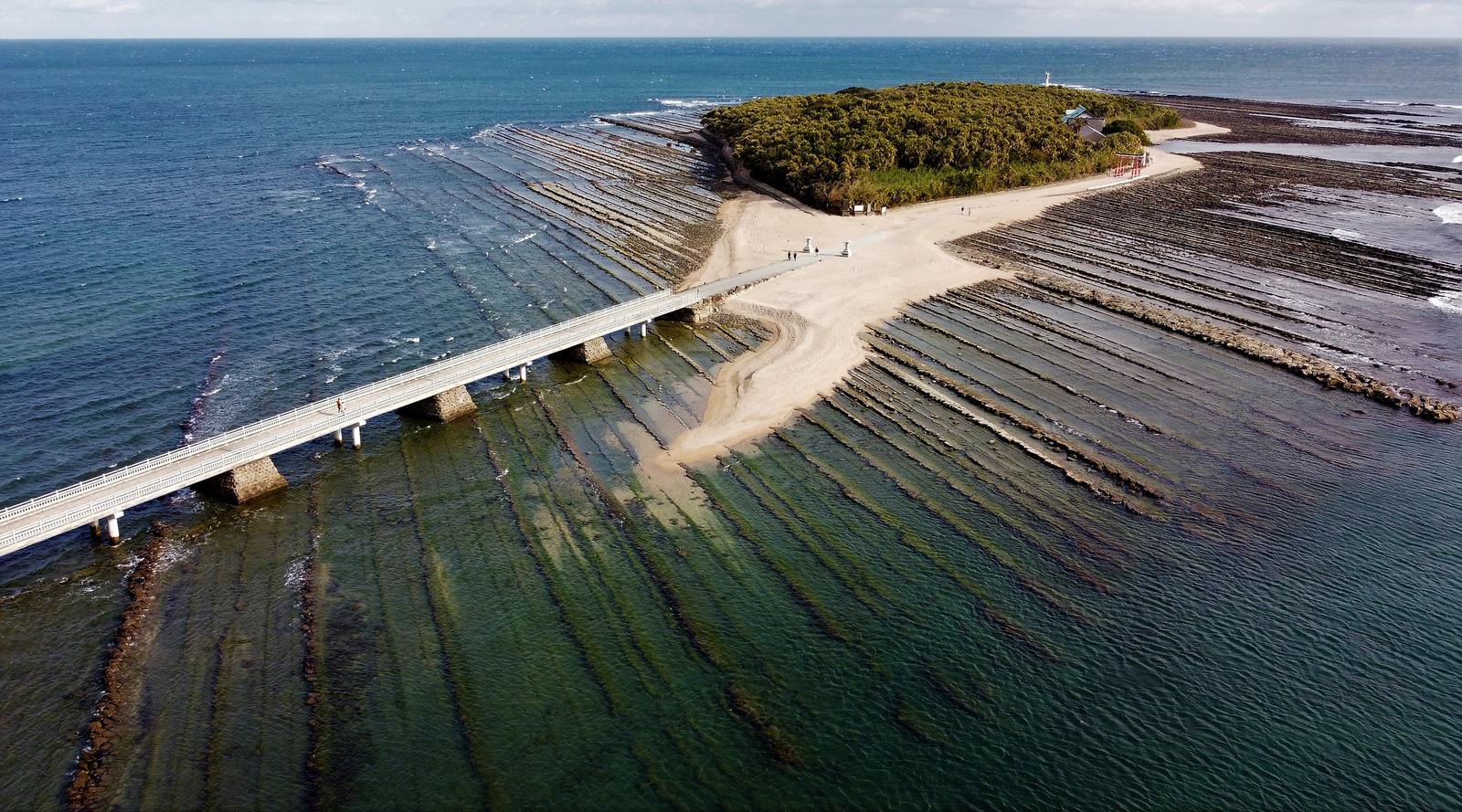 Aoshima island ringed by wave-cut rock formations, linked to the shore by a bridge